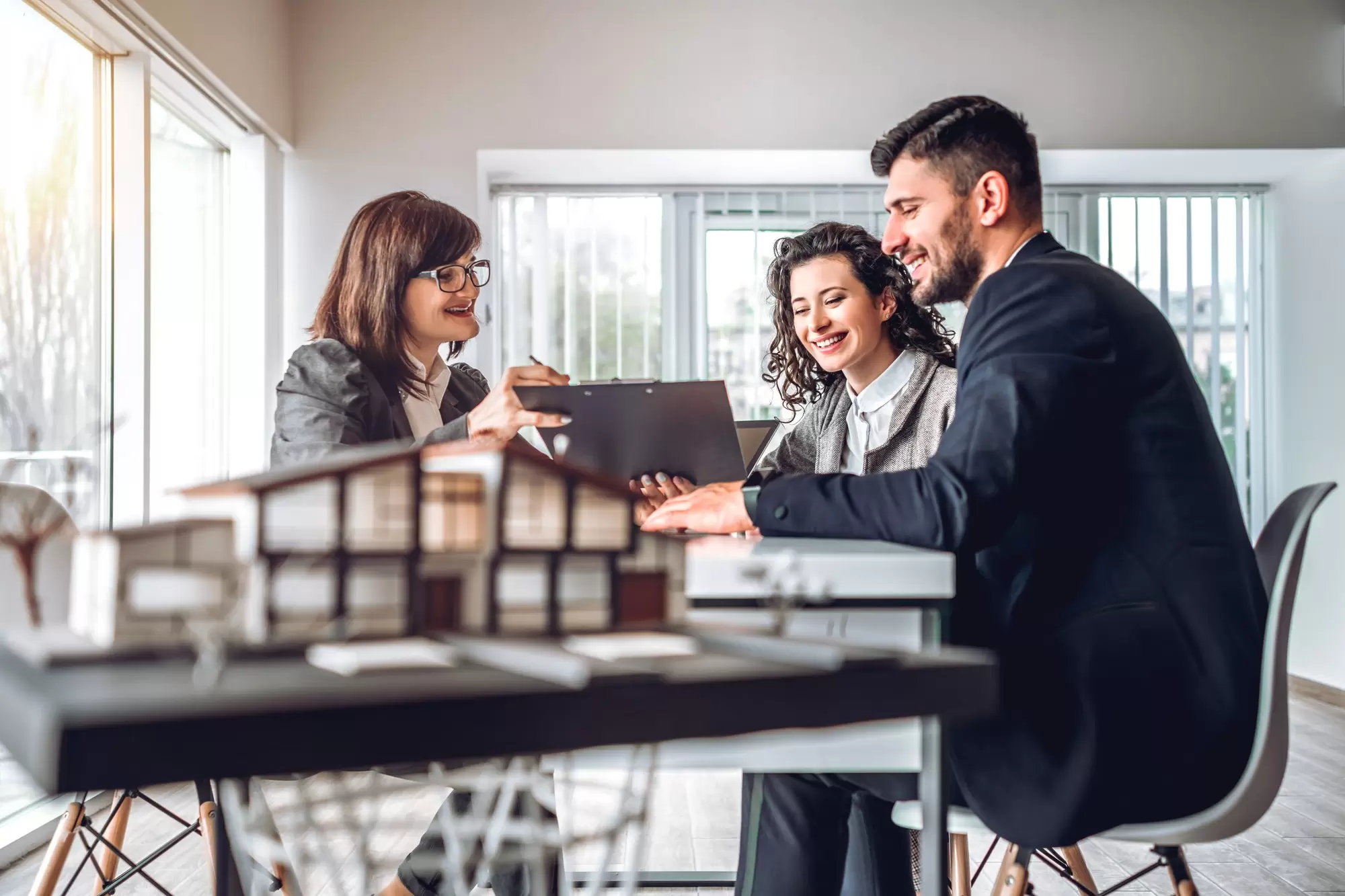 Side view image of young happy family sitting in consulting office, making property purchase. Mature realtor helping business couple do financial investment. Installment payment, mortgage loan concept.